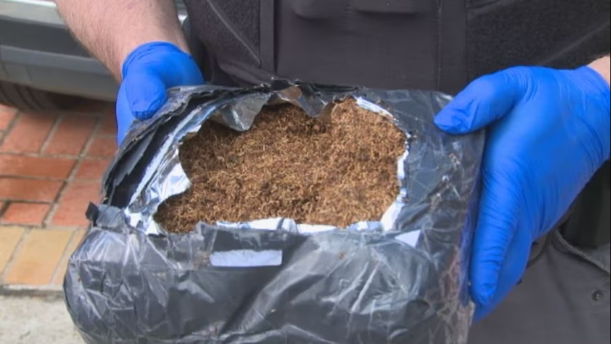 A shadowy hand-to-hand exchange of cash for an illegal, unbranded pack of cigarettes, highlighting the dangers of fake cheap tobacco in Australia.